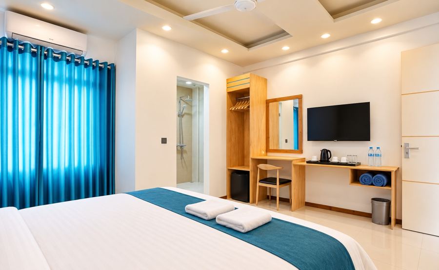 Double room with blue curtains, an air conditioner, a wooden wardrobe, desk, mirror and wall TV