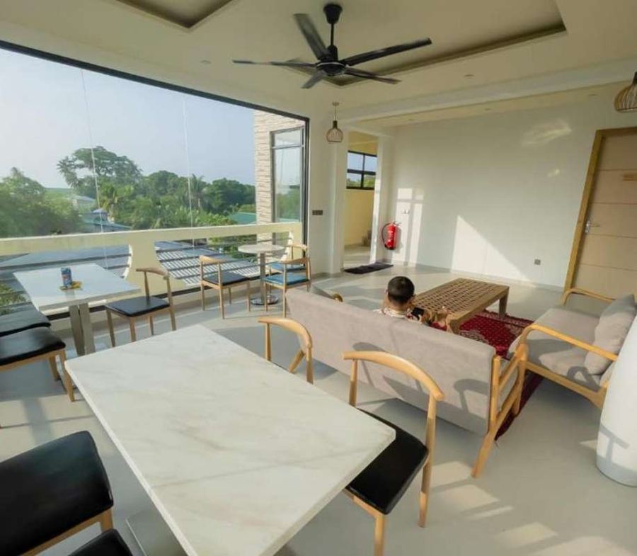 Bright terrace restaurant with marble tables, wooden chairs, a ceiling fan and glass walls looking over the island
