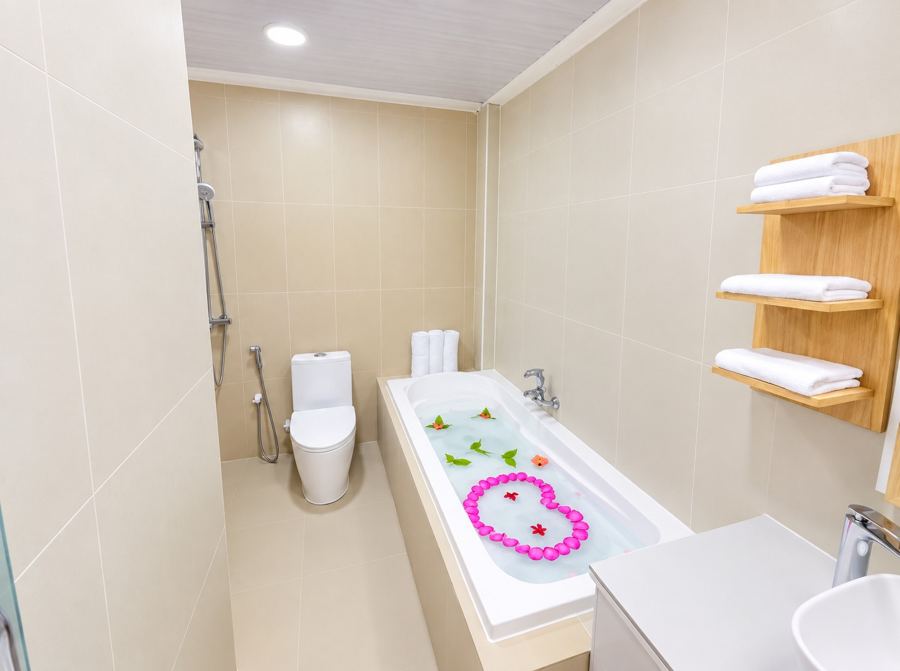 Bathroom with a bathtub decorated with flower petals, toilet, shower and wooden towel shelves