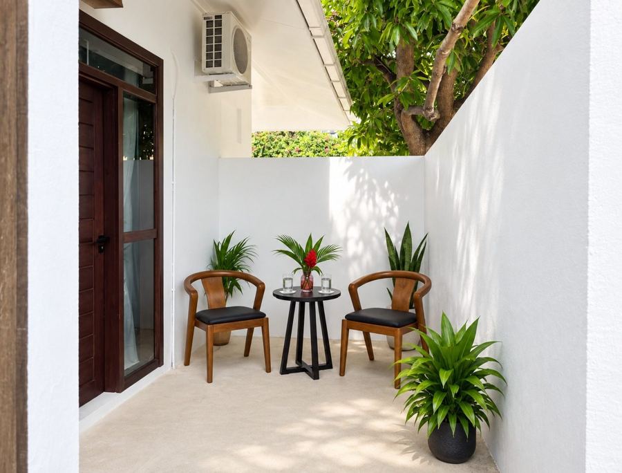 Two wooden chairs and a small round table on a white-walled terrace with potted plants