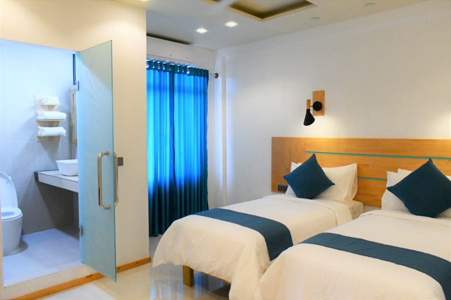 Twin beds beside a frosted glass bathroom door and blue curtains
