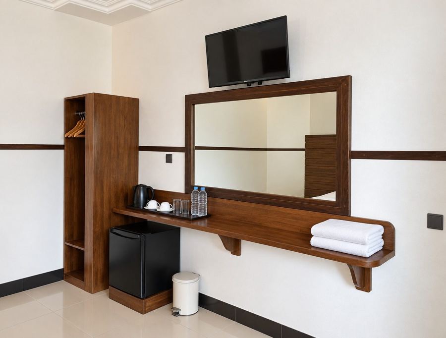 Wooden desk shelf with a kettle, cups and water bottles, a mini fridge, mirror and TV