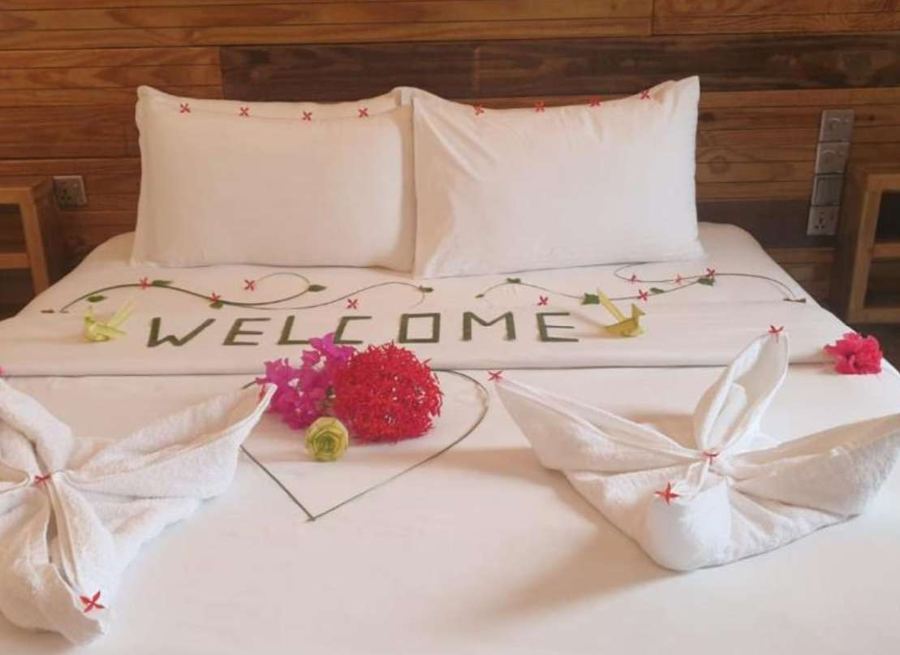 Bed with WELCOME spelled in leaves, red flowers and folded towel swans against a dark wood wall