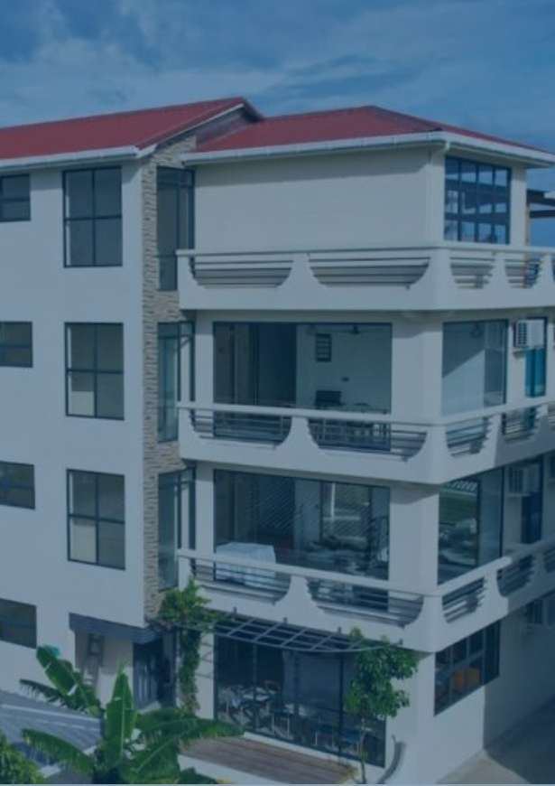 White four-storey guesthouse with balconies and a red roof, seen from above in daylight